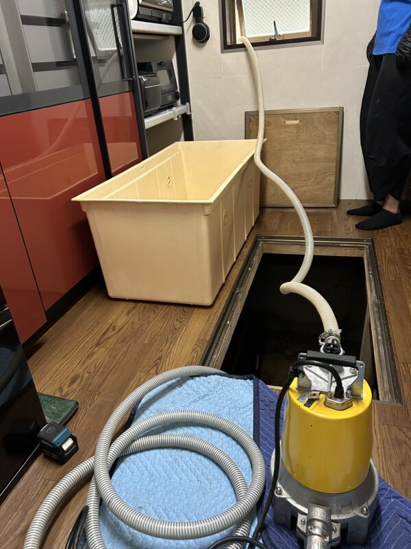 排水ポンプを用いて、キッチン床下に溜まる水を汲み出している画像